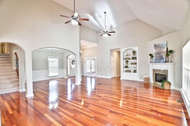 unfurnished living room featuring built in shelves, a fireplace, high vaulted ceiling, and light wood-type flooring