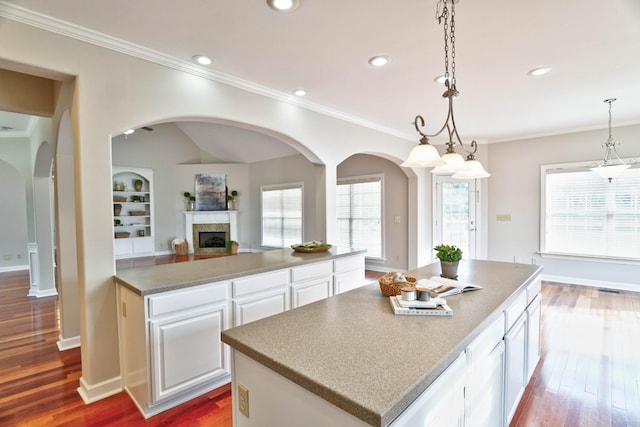 kitchen with ornamental molding, a kitchen island, hardwood / wood-style flooring, decorative light fixtures, and white cabinetry