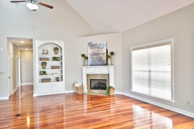 unfurnished living room featuring built in shelves, ceiling fan, high vaulted ceiling, and light hardwood / wood-style flooring