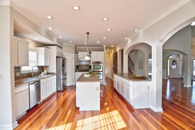 kitchen with a center island, sink, stainless steel appliances, backsplash, and pendant lighting