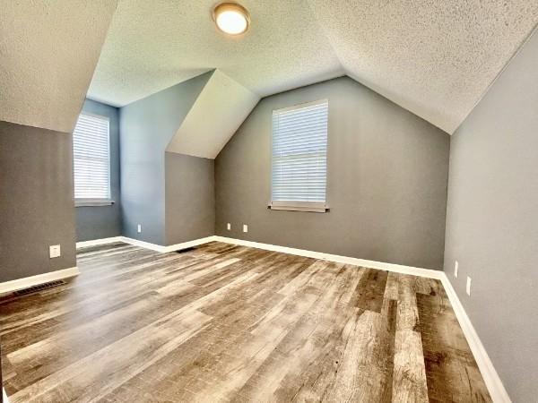 bonus room with lofted ceiling, wood-type flooring, and a textured ceiling