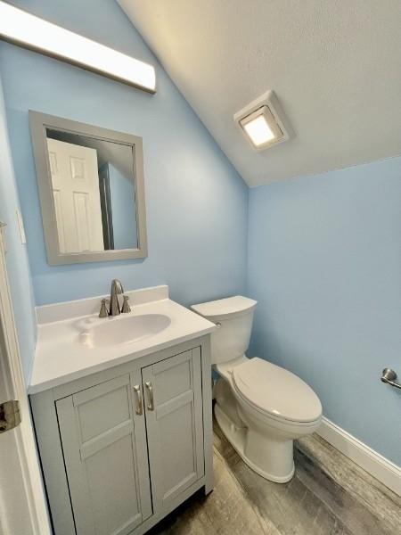 bathroom with vanity, wood-type flooring, lofted ceiling, and toilet