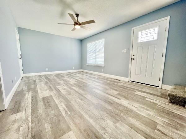 foyer entrance with plenty of natural light, ceiling fan, light wood-type flooring, and a textured ceiling