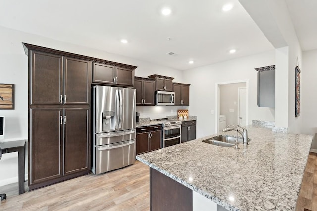 kitchen with light stone countertops, kitchen peninsula, light wood-type flooring, stainless steel appliances, and sink