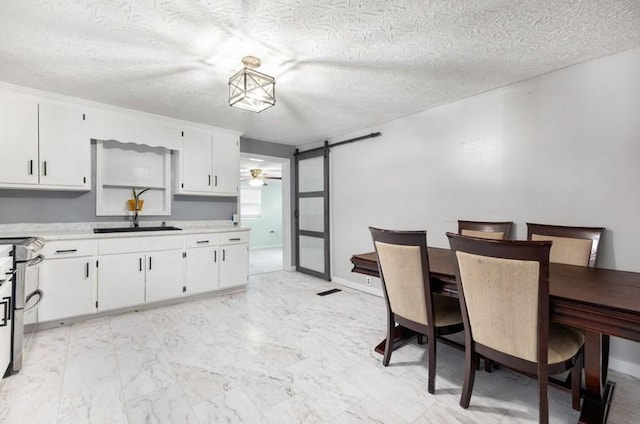 kitchen featuring a textured ceiling, ceiling fan, sink, a barn door, and white cabinets