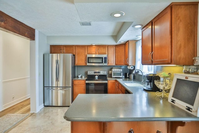 kitchen featuring a peninsula, appliances with stainless steel finishes, a sink, and brown cabinets