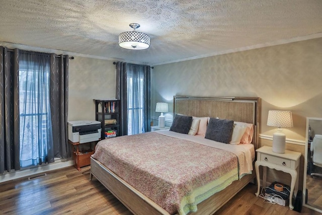 bedroom featuring a textured ceiling, ornamental molding, wood finished floors, and visible vents