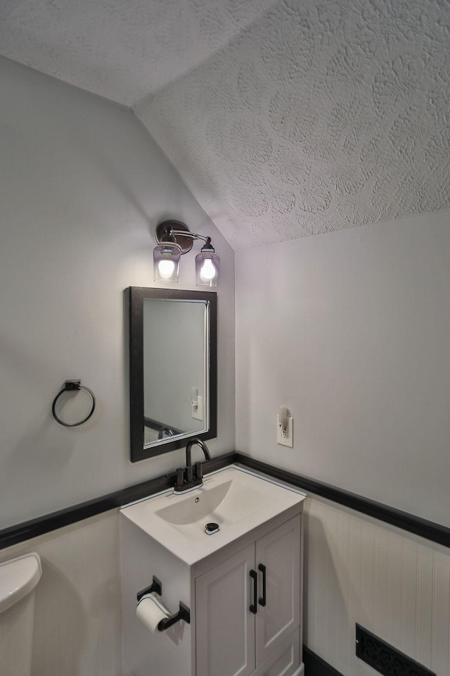 half bath with lofted ceiling, a wainscoted wall, a textured ceiling, and vanity