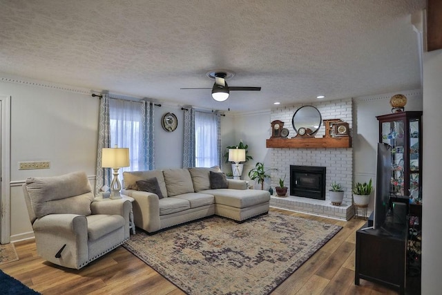 living area with a ceiling fan, a fireplace, a textured ceiling, and wood finished floors