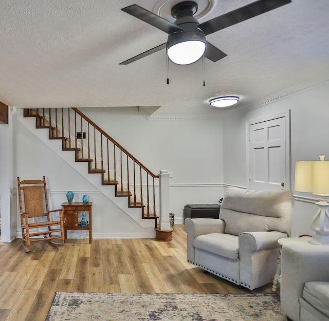 living room featuring ceiling fan, a textured ceiling, wood finished floors, baseboards, and stairs