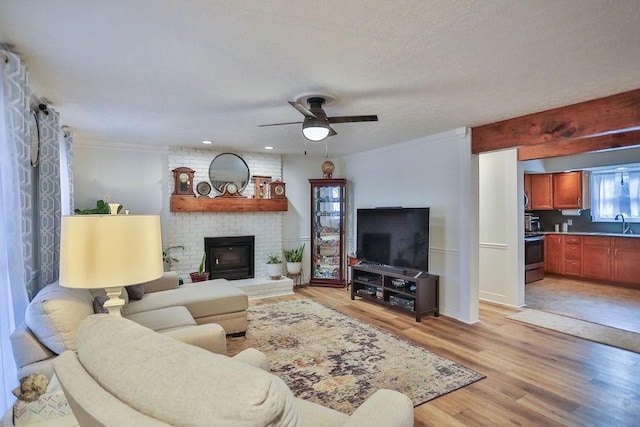 living area with ceiling fan, ornamental molding, a brick fireplace, and light wood-style flooring