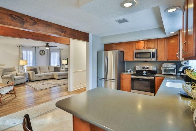 kitchen with light wood-style flooring, brown cabinets, open floor plan, a peninsula, and stainless steel appliances