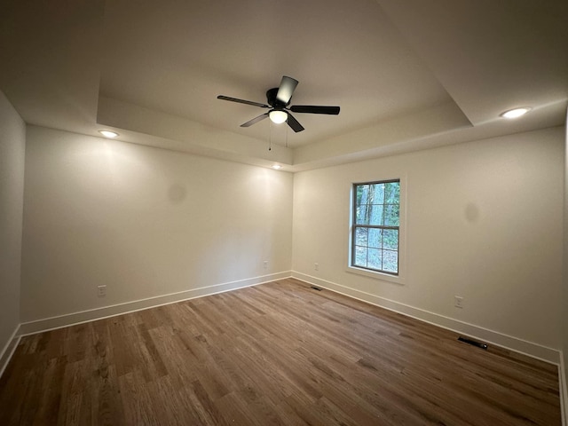 unfurnished room with ceiling fan, dark hardwood / wood-style flooring, and a tray ceiling