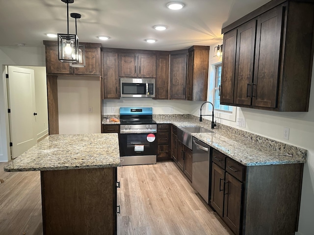 kitchen with light stone countertops, a center island, pendant lighting, light hardwood / wood-style floors, and appliances with stainless steel finishes