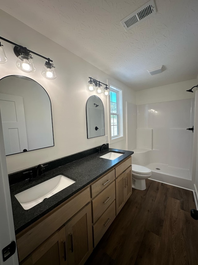 bathroom with a textured ceiling, vanity, a shower, hardwood / wood-style floors, and toilet