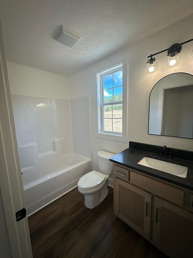 full bathroom with vanity, a textured ceiling, hardwood / wood-style flooring, washtub / shower combination, and toilet