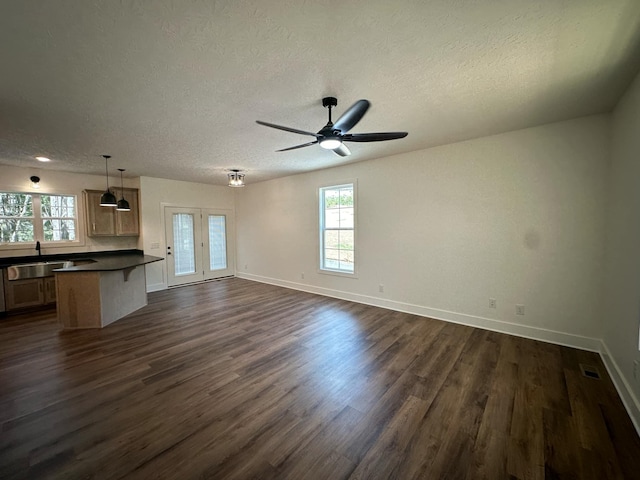 unfurnished living room featuring ceiling fan, dark hardwood / wood-style flooring, a healthy amount of sunlight, and a textured ceiling