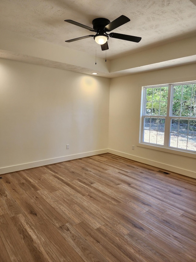 empty room with ceiling fan, wood-type flooring, and a textured ceiling