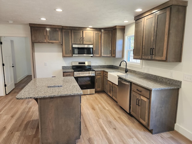 kitchen with light stone countertops, appliances with stainless steel finishes, light hardwood / wood-style flooring, and sink