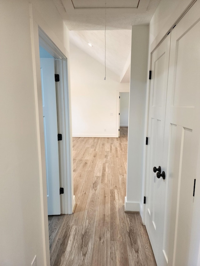 hall featuring light hardwood / wood-style floors, a textured ceiling, and vaulted ceiling