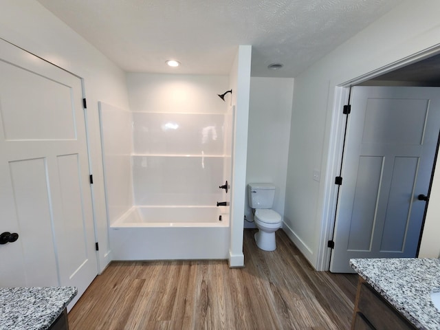 full bathroom featuring hardwood / wood-style floors, a textured ceiling, toilet, vanity, and bathtub / shower combination