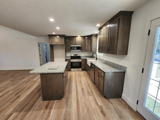 kitchen featuring a center island, dark brown cabinets, light hardwood / wood-style floors, light stone counters, and stainless steel appliances