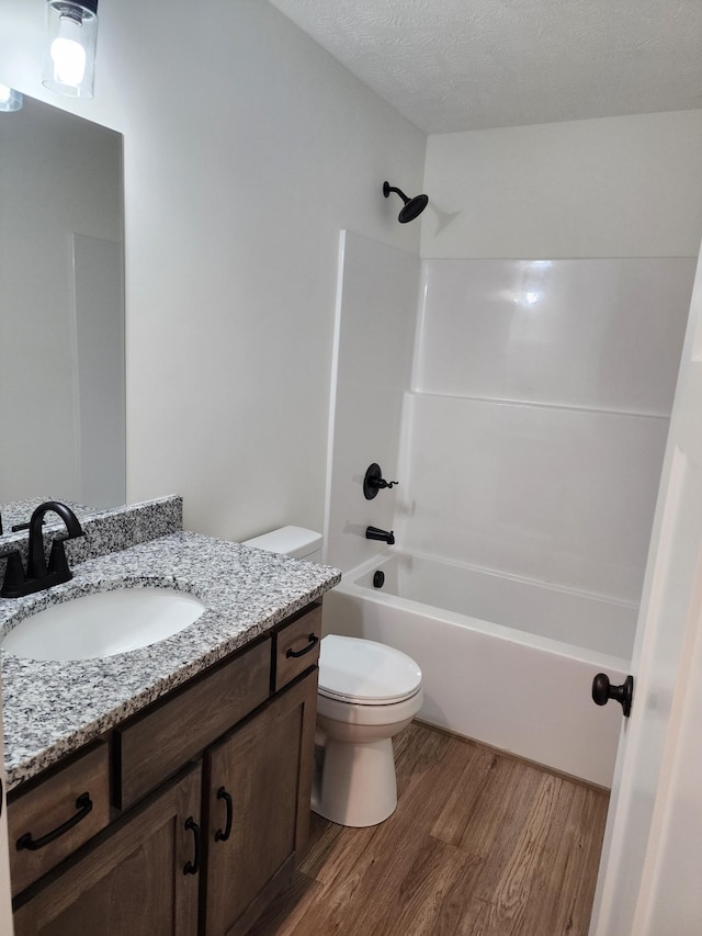 full bathroom with wood-type flooring,  shower combination, a textured ceiling, toilet, and vanity