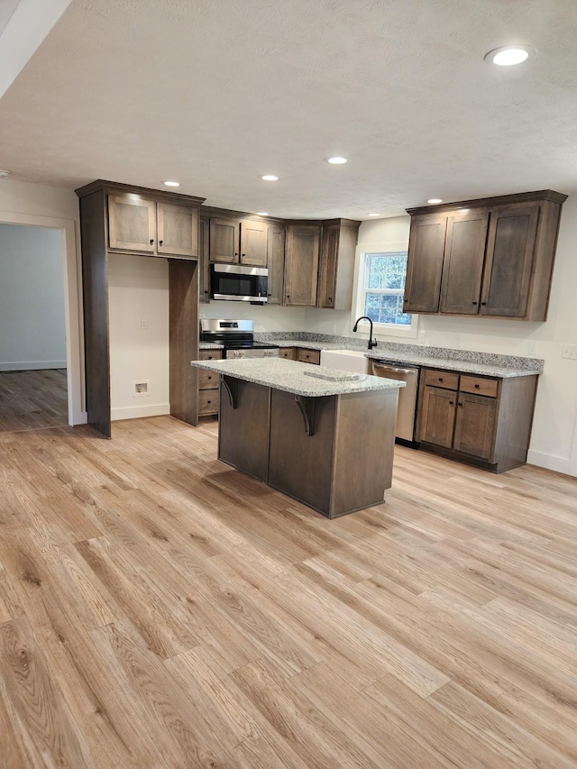 kitchen featuring light stone countertops, a center island, stainless steel appliances, a kitchen breakfast bar, and light wood-type flooring