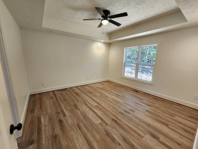 empty room with hardwood / wood-style floors, a textured ceiling, and a tray ceiling