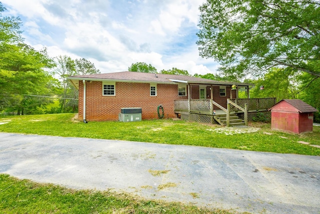 rear view of property featuring a wooden deck, a yard, and a storage shed