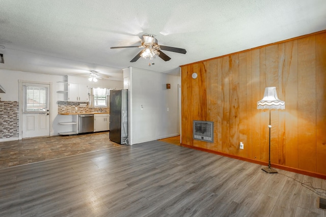 unfurnished living room featuring wood walls, dark wood-type flooring, ceiling fan, a textured ceiling, and heating unit