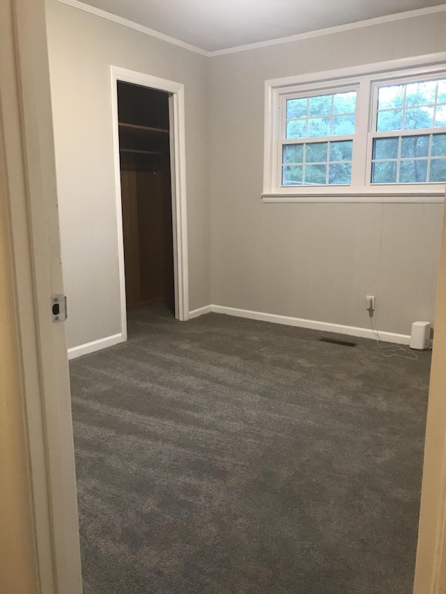 unfurnished bedroom featuring dark colored carpet, ornamental molding, and a closet