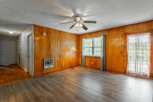 spare room with heating unit, ceiling fan, crown molding, hardwood / wood-style flooring, and wood walls