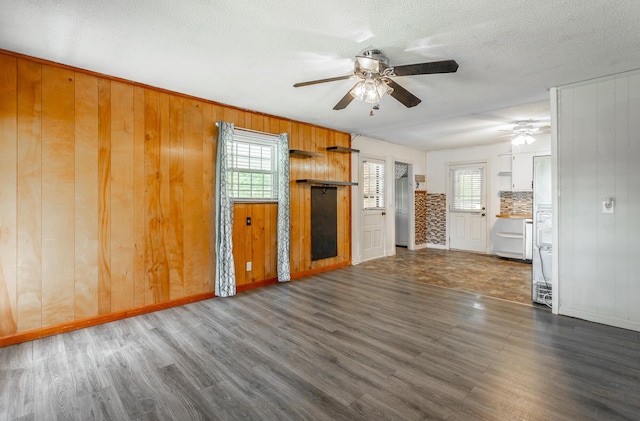 unfurnished living room featuring a textured ceiling, ceiling fan, dark wood-type flooring, and wood walls