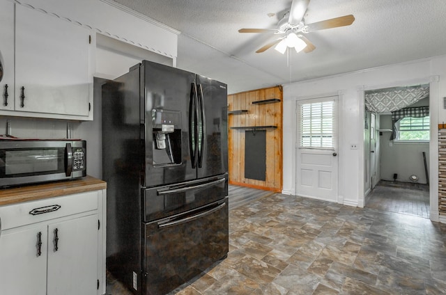 kitchen featuring black refrigerator with ice dispenser, a textured ceiling, ceiling fan, wooden walls, and white cabinetry