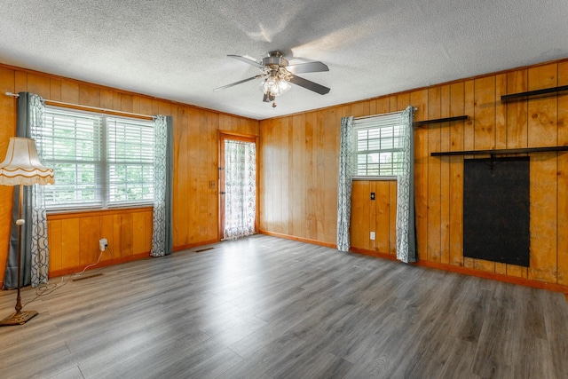 unfurnished living room with a textured ceiling, ceiling fan, hardwood / wood-style floors, and wood walls