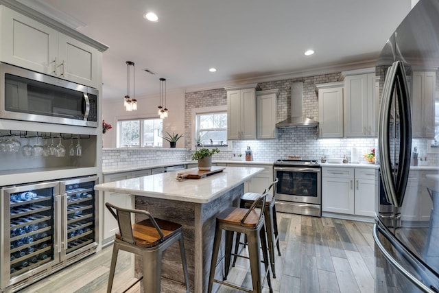 kitchen with backsplash, stainless steel appliances, beverage cooler, wall chimney range hood, and pendant lighting