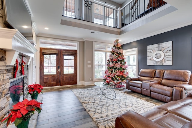 living room with a stone fireplace, french doors, wood-type flooring, and ornamental molding