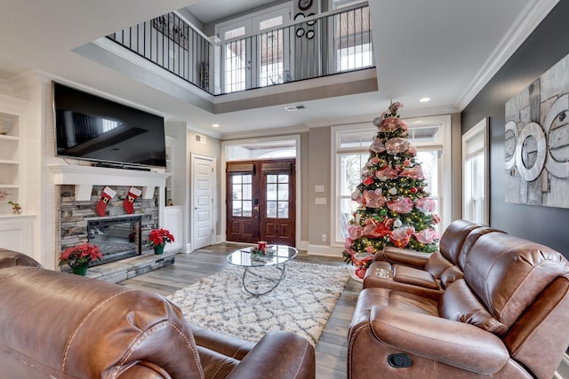 living room with built in shelves, hardwood / wood-style flooring, a stone fireplace, and ornamental molding