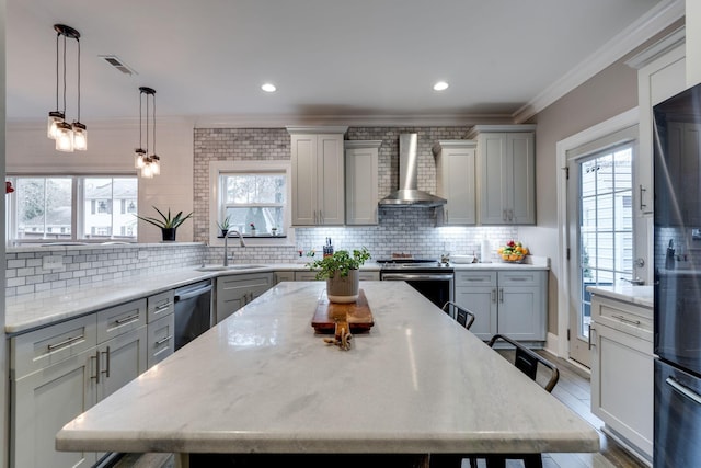 kitchen with a kitchen bar, stainless steel appliances, plenty of natural light, and wall chimney exhaust hood