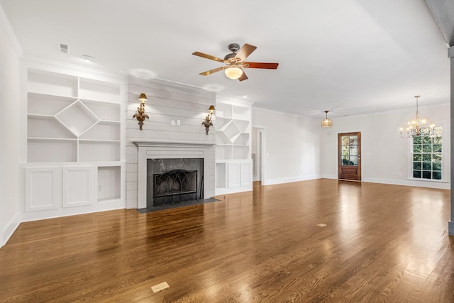 unfurnished living room with ceiling fan with notable chandelier, built in features, crown molding, hardwood / wood-style flooring, and a premium fireplace