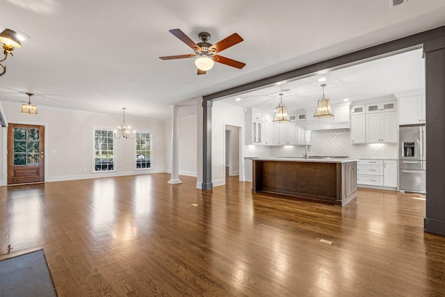 unfurnished living room with sink, ornate columns, ornamental molding, dark hardwood / wood-style flooring, and ceiling fan with notable chandelier