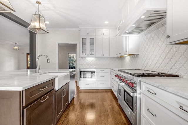 kitchen featuring decorative light fixtures, white cabinets, light stone counters, stainless steel appliances, and wall chimney range hood