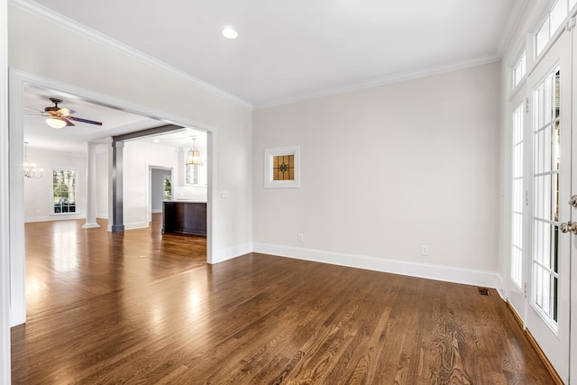 unfurnished room featuring ornamental molding, ceiling fan with notable chandelier, dark wood-type flooring, and decorative columns