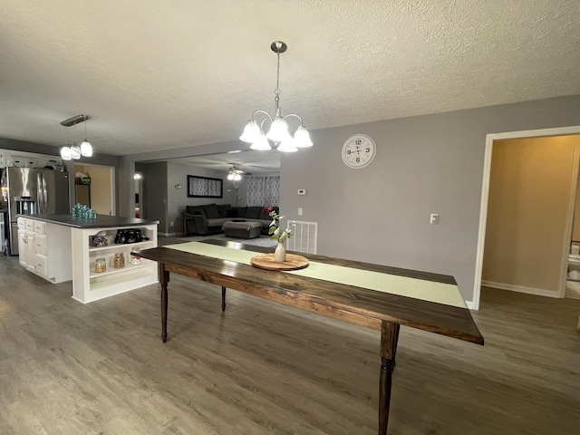 dining room with dark wood-style floors, visible vents, a textured ceiling, and an inviting chandelier