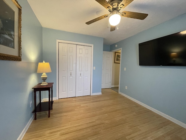 bedroom featuring baseboards, ceiling fan, a textured ceiling, light wood-style floors, and a closet