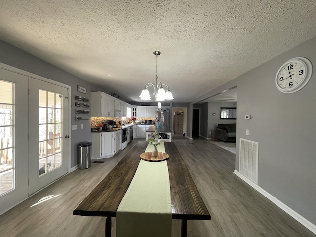 dining area featuring dark wood-style floors, a textured ceiling, visible vents, and a notable chandelier