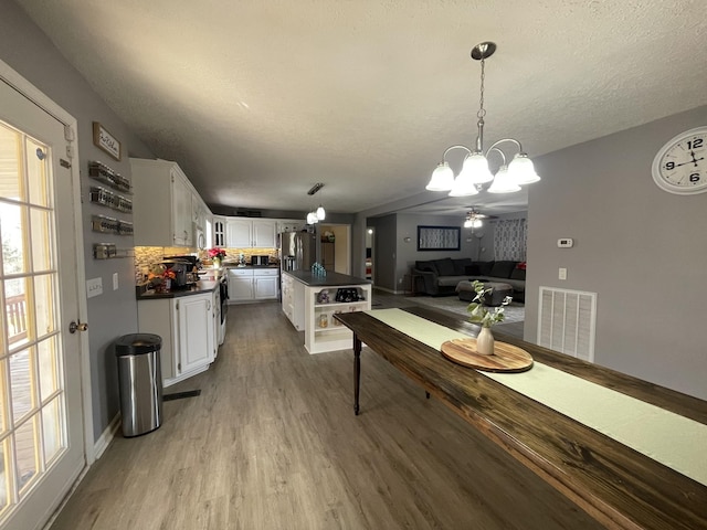 dining space featuring visible vents, a notable chandelier, a textured ceiling, and wood finished floors