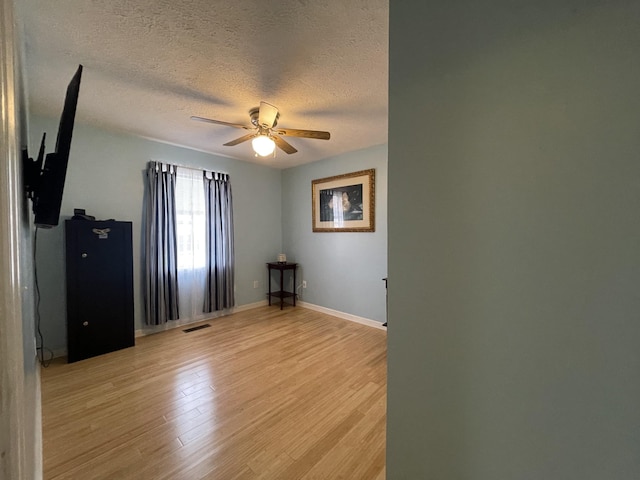 unfurnished room with a textured ceiling, light wood-style flooring, visible vents, baseboards, and a ceiling fan