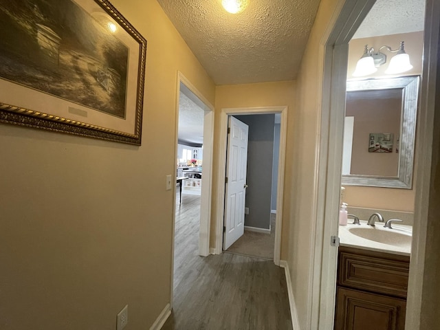 hallway with a textured ceiling, a sink, dark wood finished floors, and baseboards